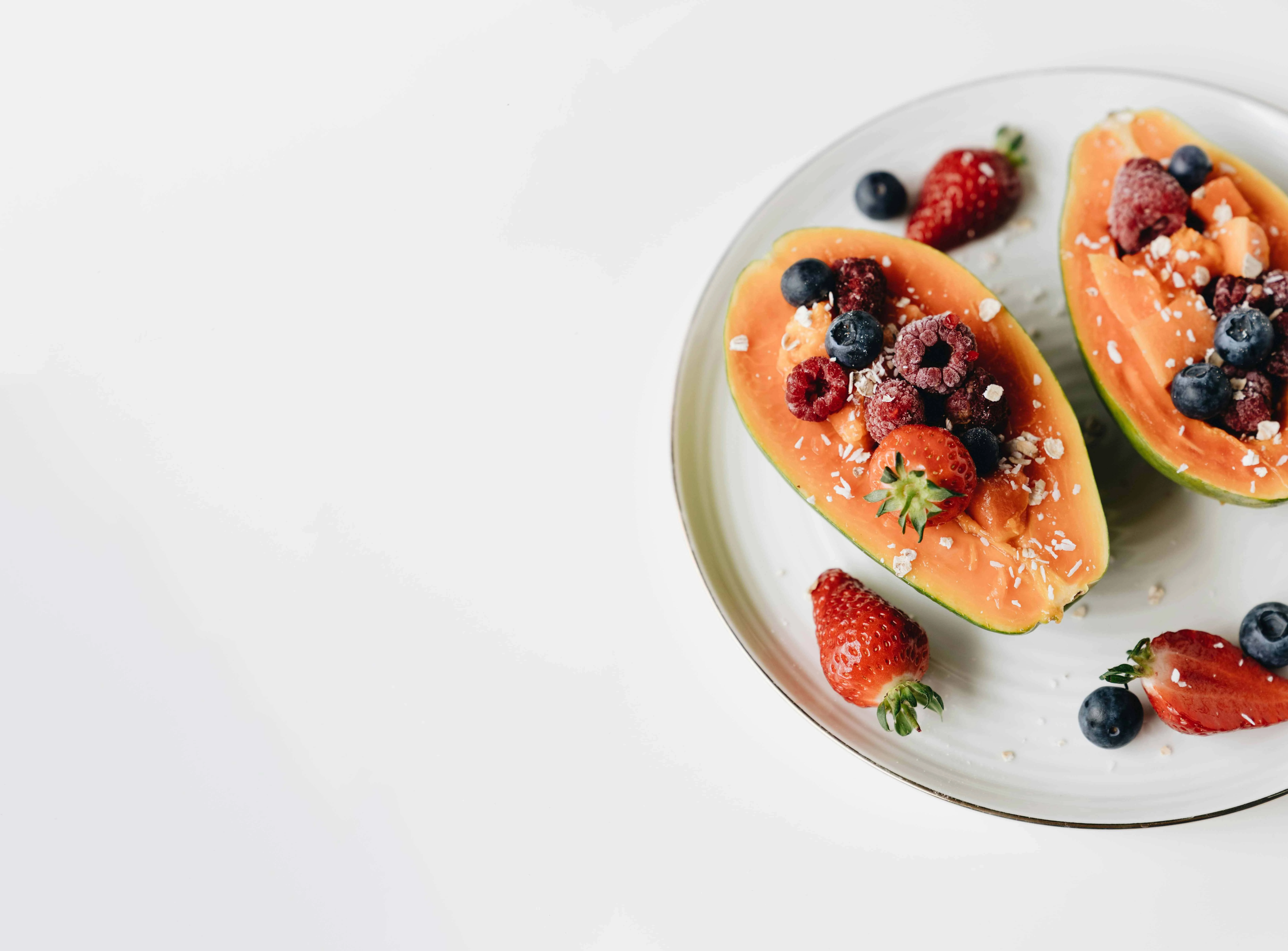 Papaya halves topped with fresh berries and oats on a white plate